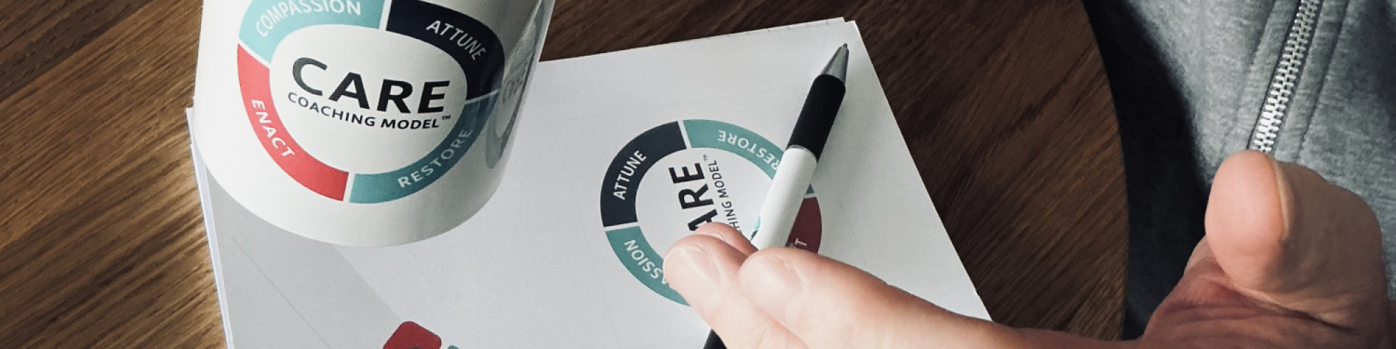 A person sits at a table with a mug, notebook, pen with the CARE Coaching Model™ logo on.