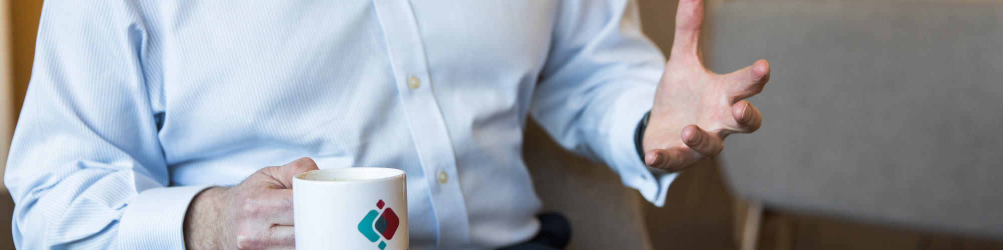 Man in blue shirt, with a mug in hand talking