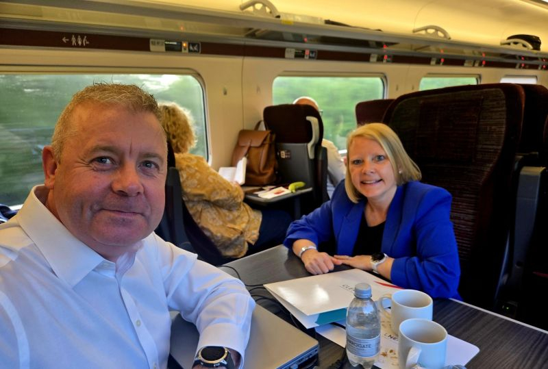 A man with a white shirt on, and a woman with a blue jacket on sat on a train.