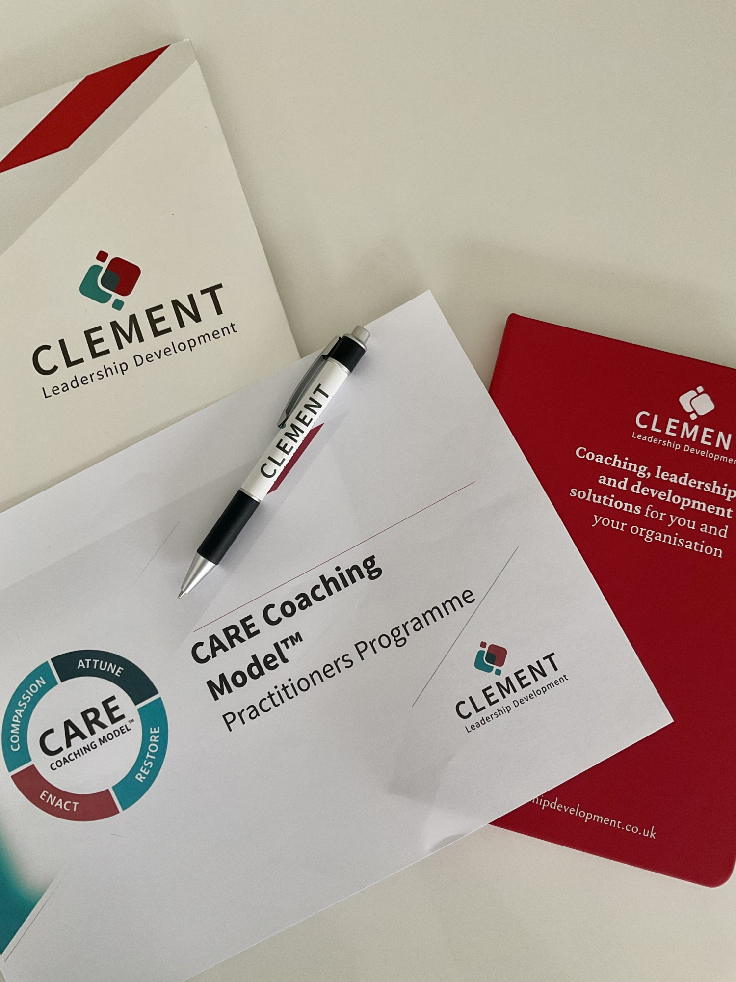 A flat lay featuring Clement Leadership Development materials, including a branded folder, pen, and programme document titled “CARE Coaching Model™ Practitioners Programme.” The CARE Coaching Model circular logo appears prominently, representing professio